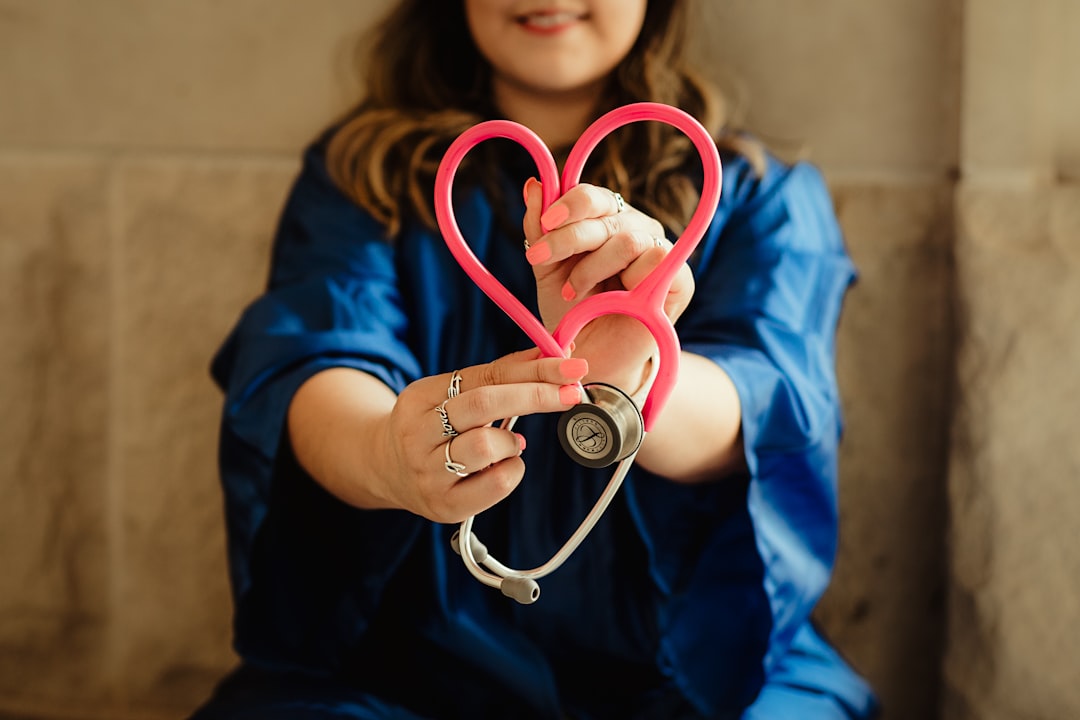 Healthcare worker in blue scrubs holding a pink stethoscope shaped into a heart