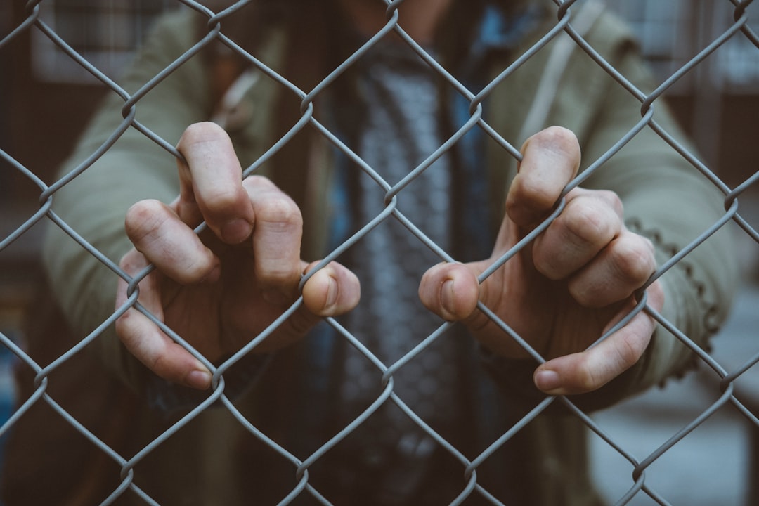 Person gripping a chain-link fence, symbolizing barriers and being trapped